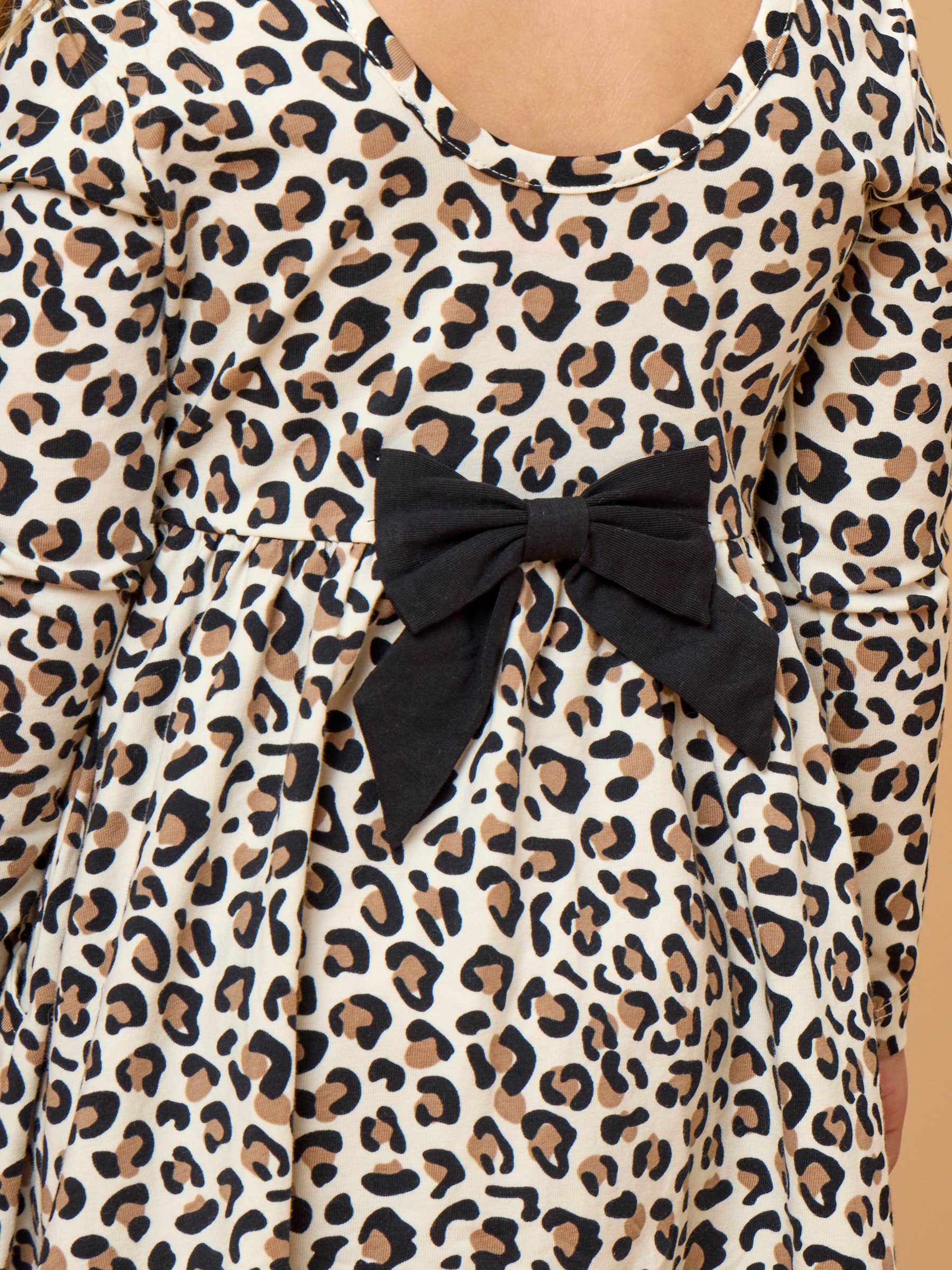 Close-up of a leopard print dress with a large black bow at the waist, featuring a warm cream background with brown and black spots.