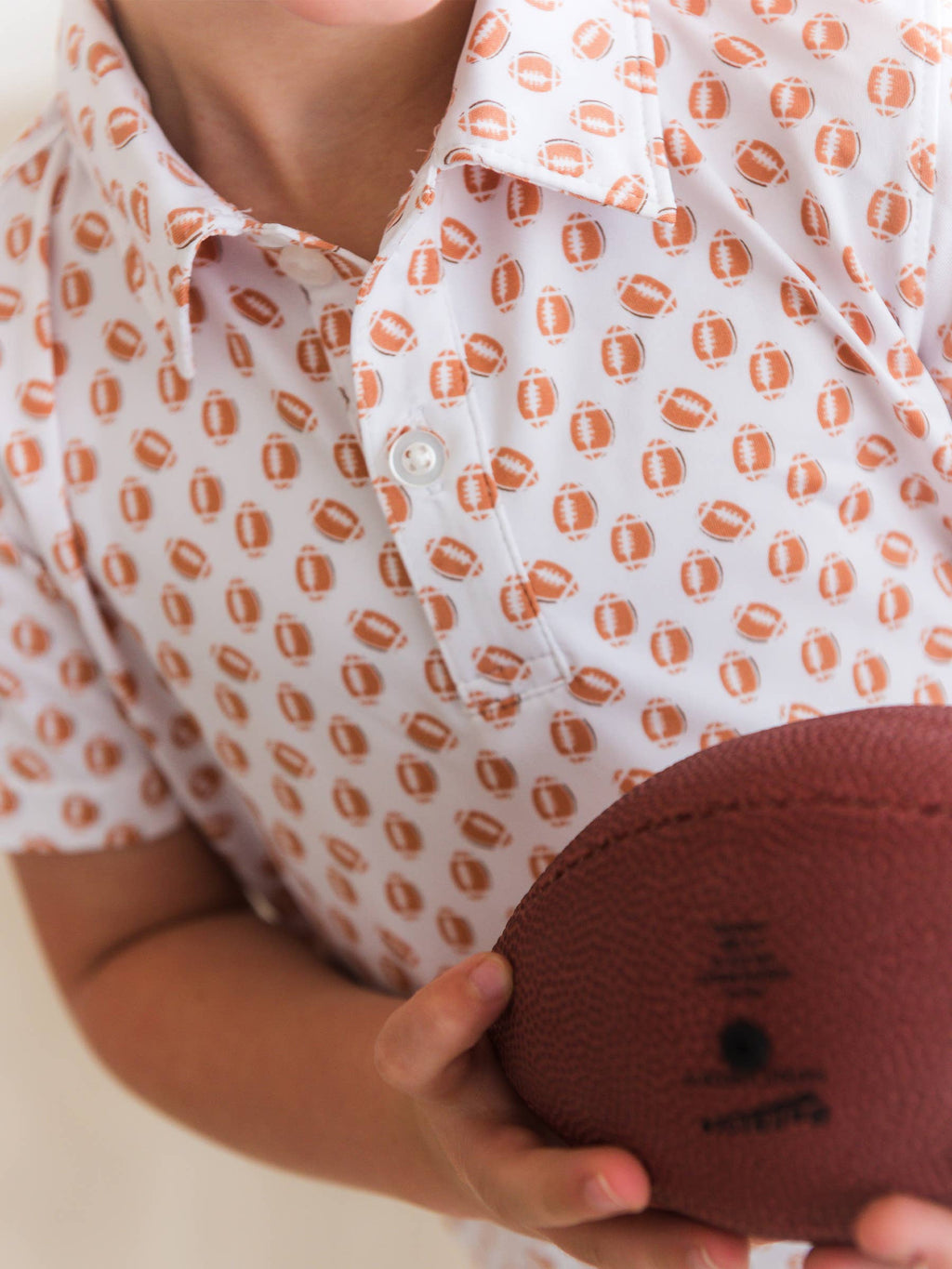 Person wearing a white shirt with orange patterns holding a brown round object.