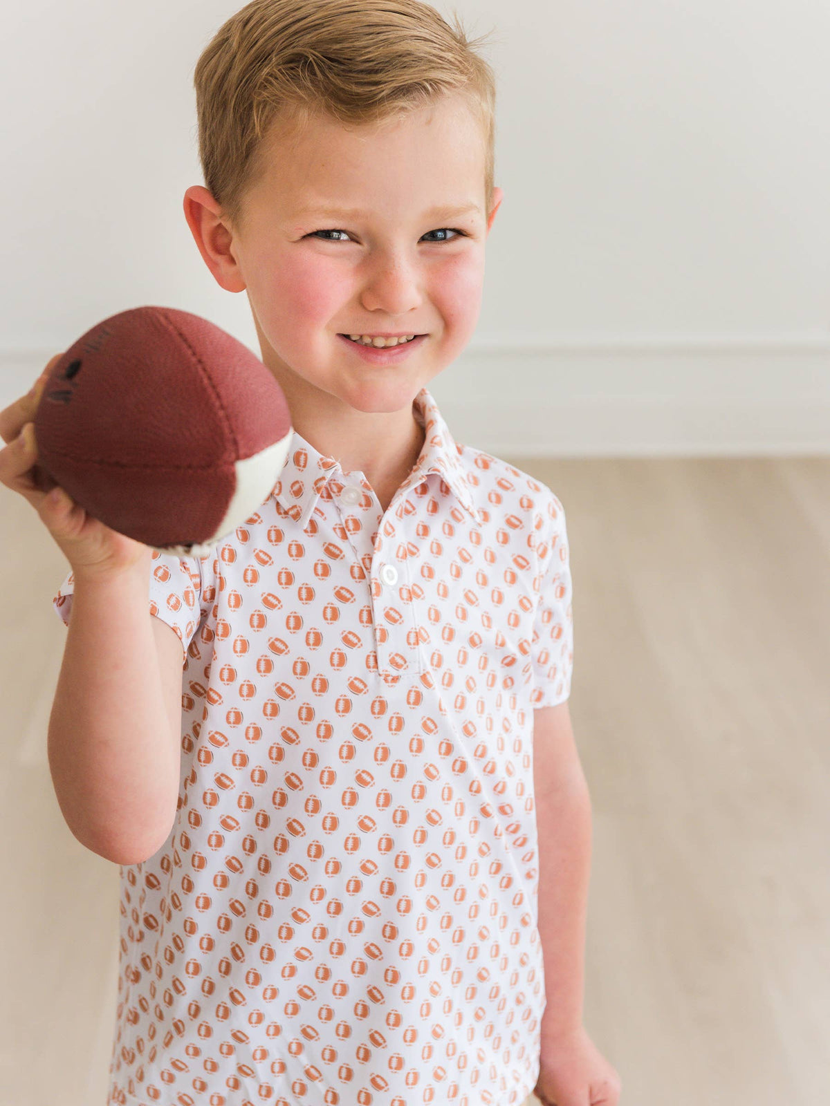 Young boy holding a red ball, wearing a patterned shirt indoors.