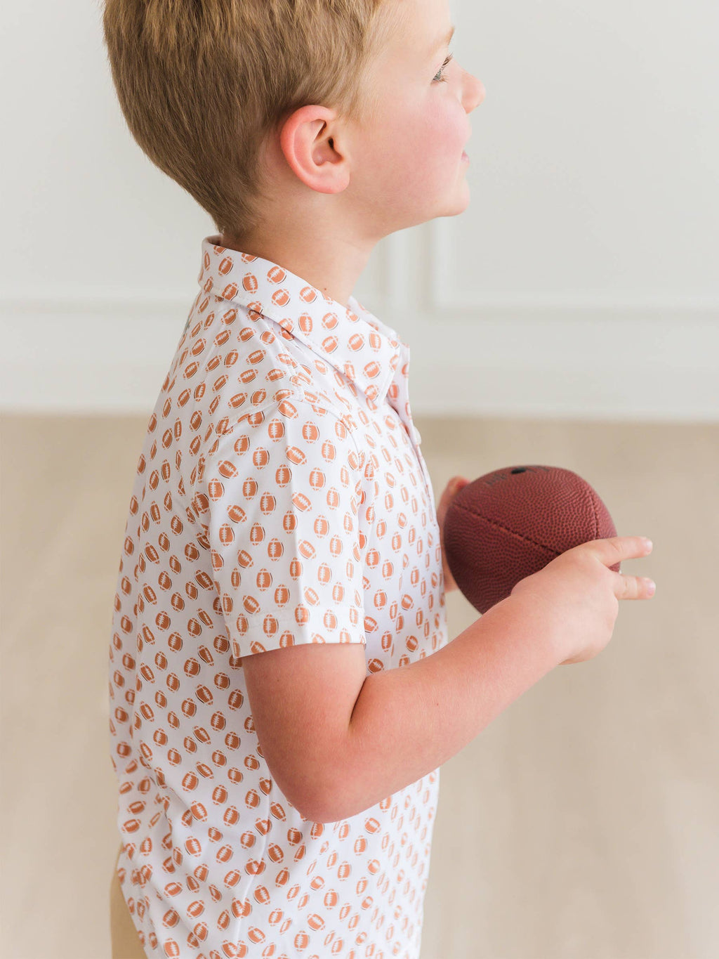 Child holding a red ball wearing a white shirt with orange patterns.
