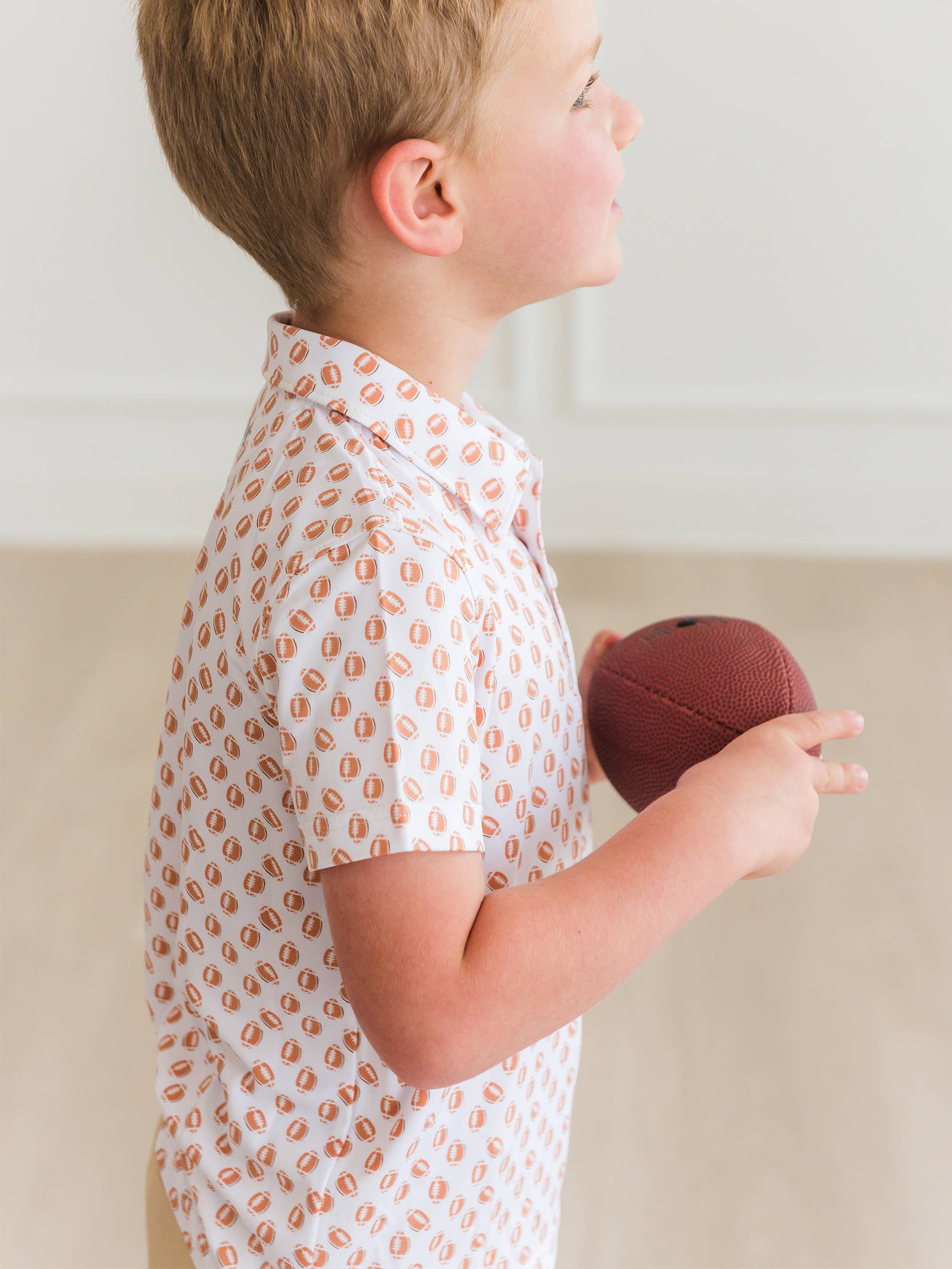 Child holding a red ball wearing a white shirt with orange patterns.