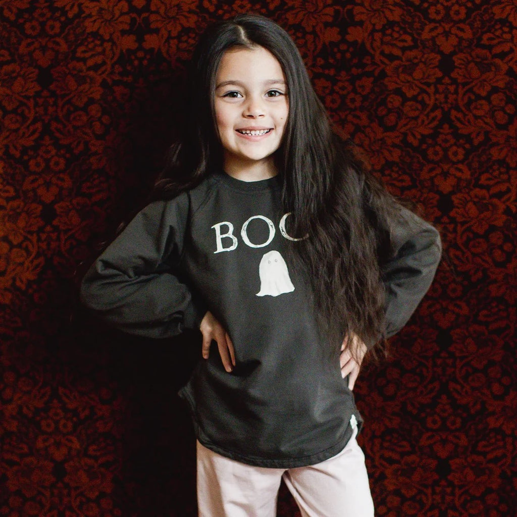 Child wearing a black organic cotton sweatshirt with 'BOO' and a ghost graphic on a red patterned background