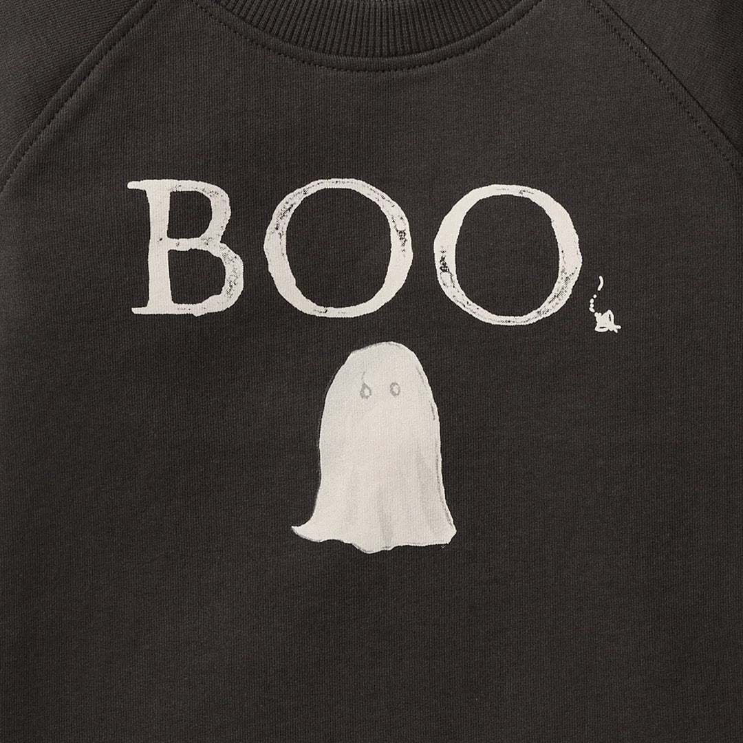 Close-up of a black toddler organic sweatshirt featuring a white distressed graphic that reads 'BOO' above a simple ghost illustration