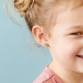 Close-up of a child wearing rainbow-shaped earrings against a light blue background