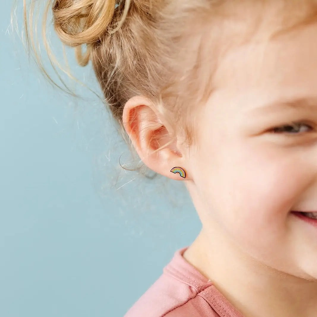 Close-up of a child wearing rainbow-shaped earrings against a light blue background