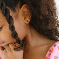 Close-up of a woman wearing a strawberry-themed earring with a child's hand on her chin.