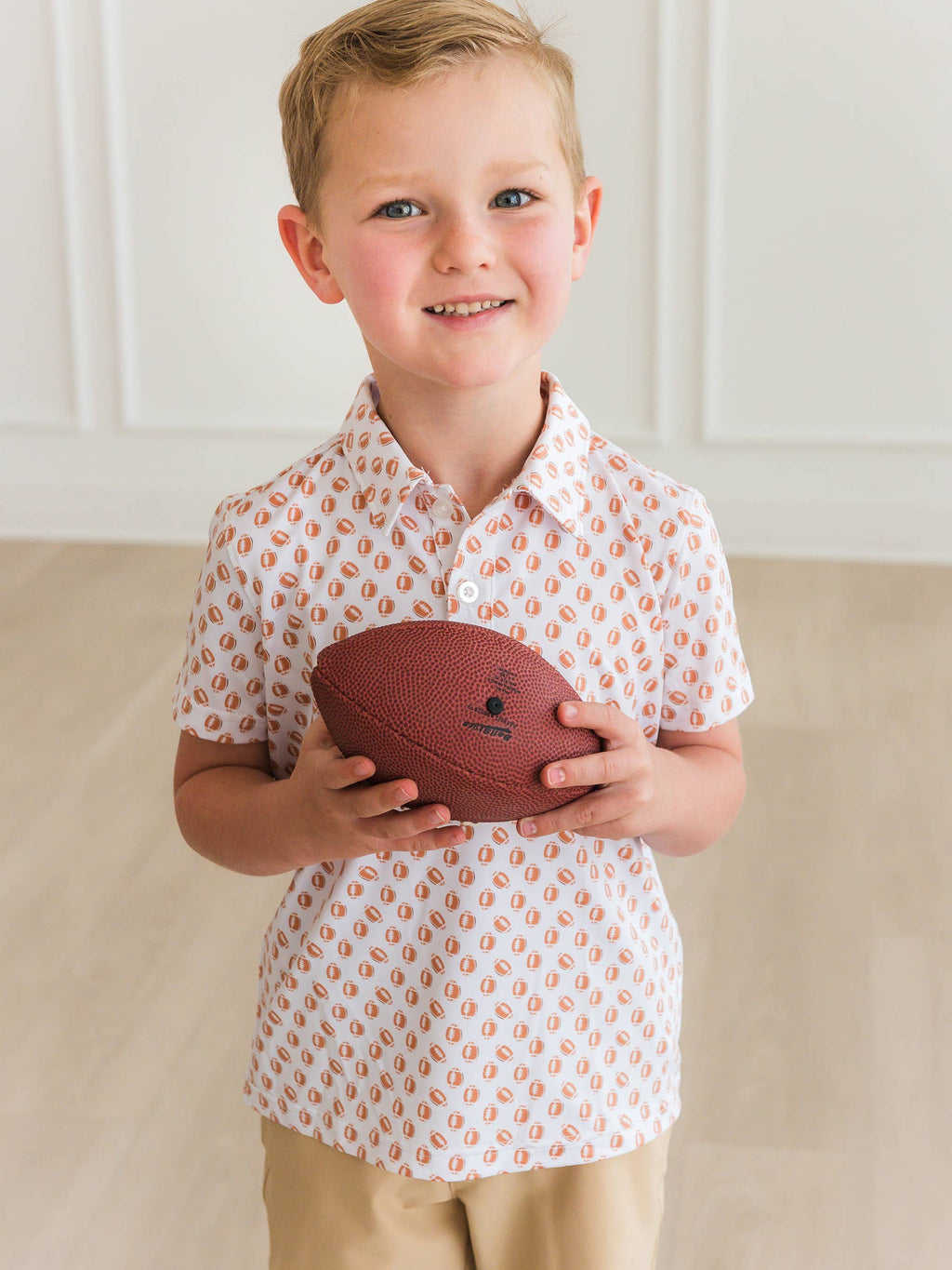 Young boy holding a football indoors with a neutral background
